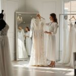 Nevesta drží čipkované svadobné šaty pred zrkadlom v svetlom svadobnom salóne.