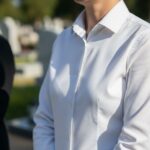 Detail osoby v bielej košeli na pohrebe s rozmazaným cintorínom v pozadí