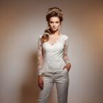 Nevesta v modernom bielom nohavicovom kostýme s prirodzeným líčením a účesom s kvetinovou ozdobou.