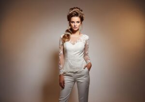 Nevesta v modernom bielom nohavicovom kostýme s prirodzeným líčením a účesom s kvetinovou ozdobou.