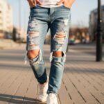 Mladá osoba v roztrhaných džínsach, biele tenisky a tričko, mestský štýl na slnečnom dni