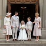 Rodina na prvej svätej omši pred kostolom, dievča v bielych šatách s venčekom, hostia v jarnom oblečení.