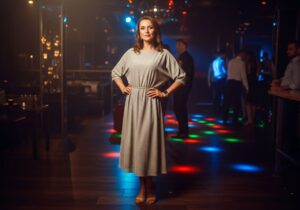 Žena v štýlových šatách stojí v modernom nočnom klube s farebnými svetlami na pozadí.