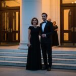 Elegantný pár pred koncertnou halou večer v formálnom oblečení s osvetlením a schodmi v pozadí