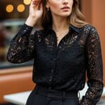 Žena v čiernej čipkovanej blúzke stojaca v kaviarni, jemné svetlo zvýrazňuje vzory čipky.